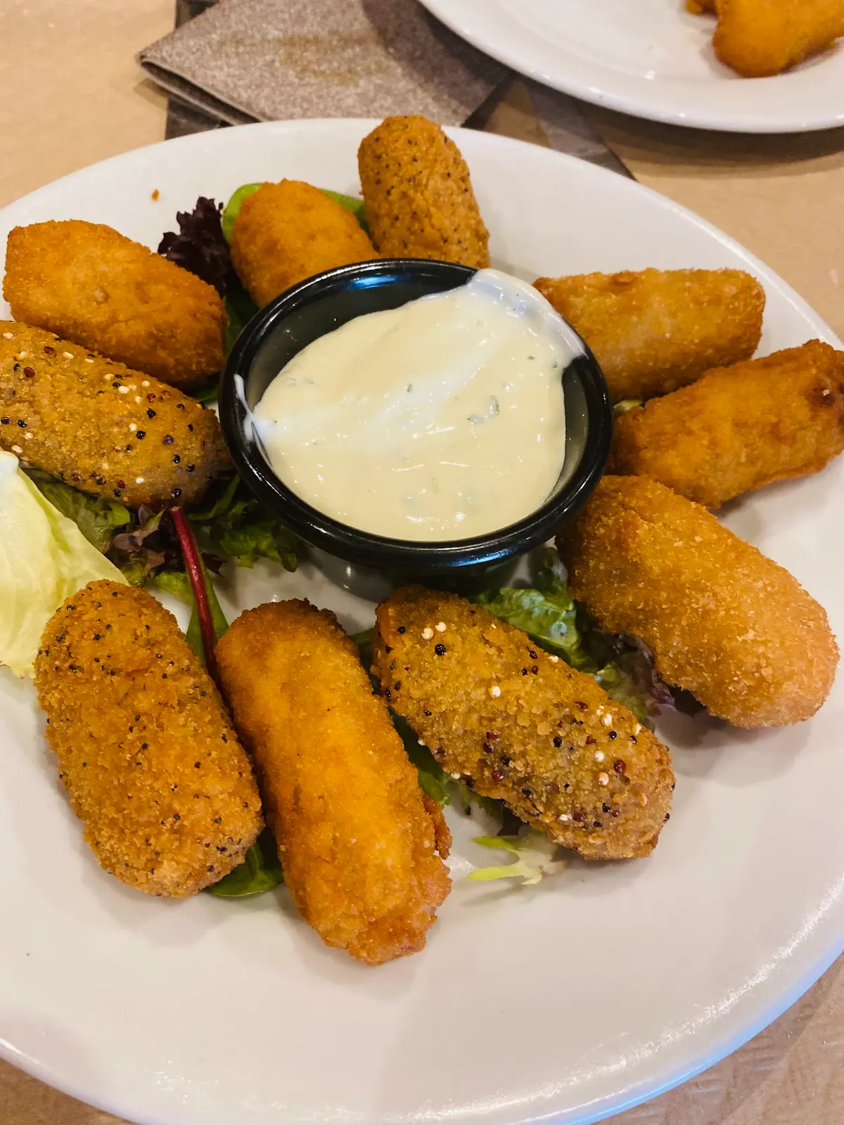 Plato de croquetas variadas alrededor de un cuenco de salsa, sobre unas hojas de lechuga