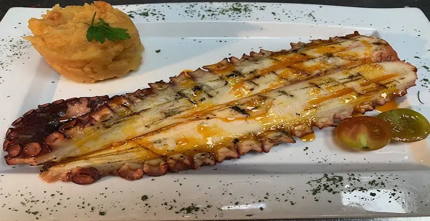 Pata de pulpo a la parrilla abierta a lo largo, con aceite de pimentón, puré de patata y tomates cherry